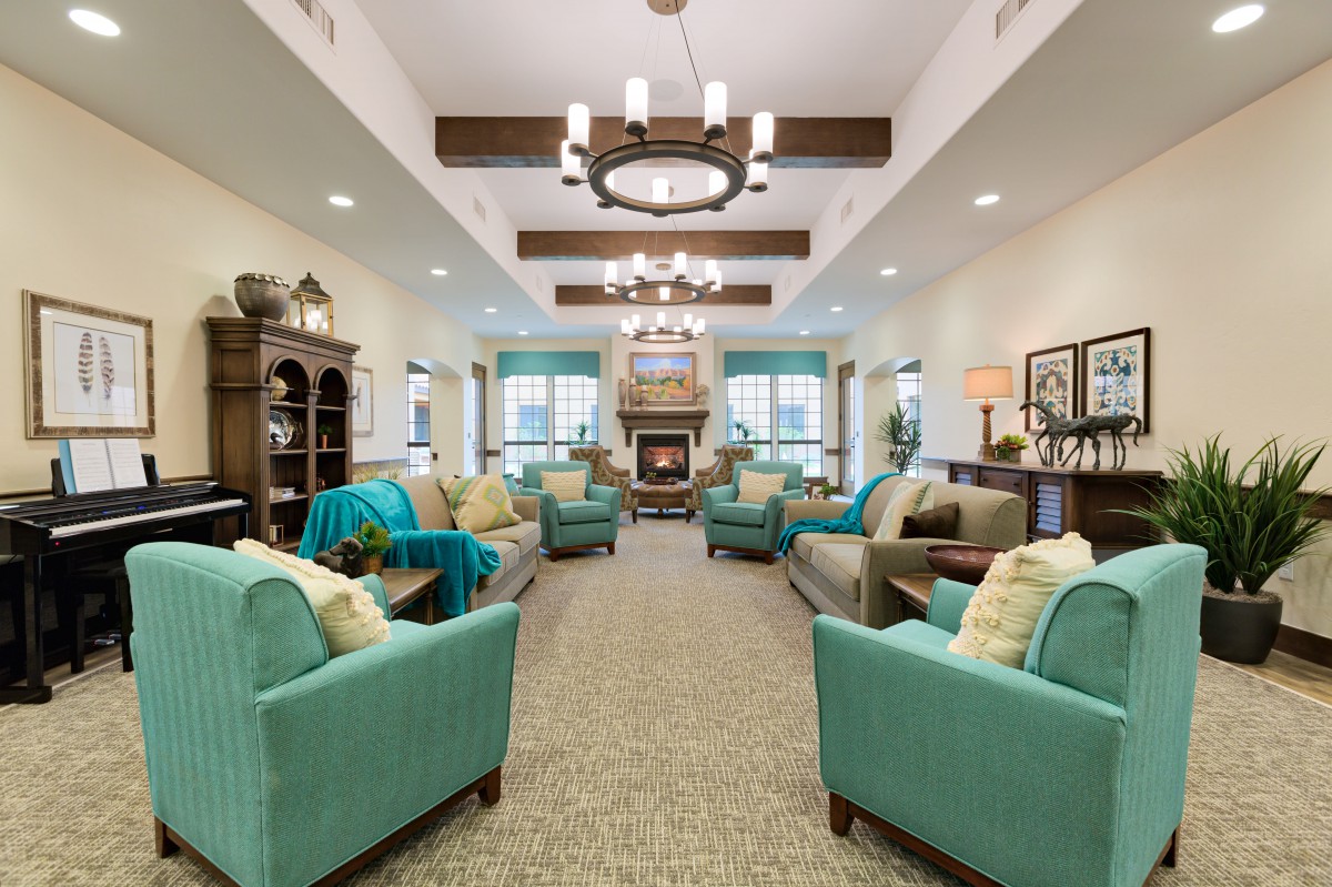A spacious and elegantly designed living room featuring teal armchairs, a central fireplace, and a stylish chandelier.
