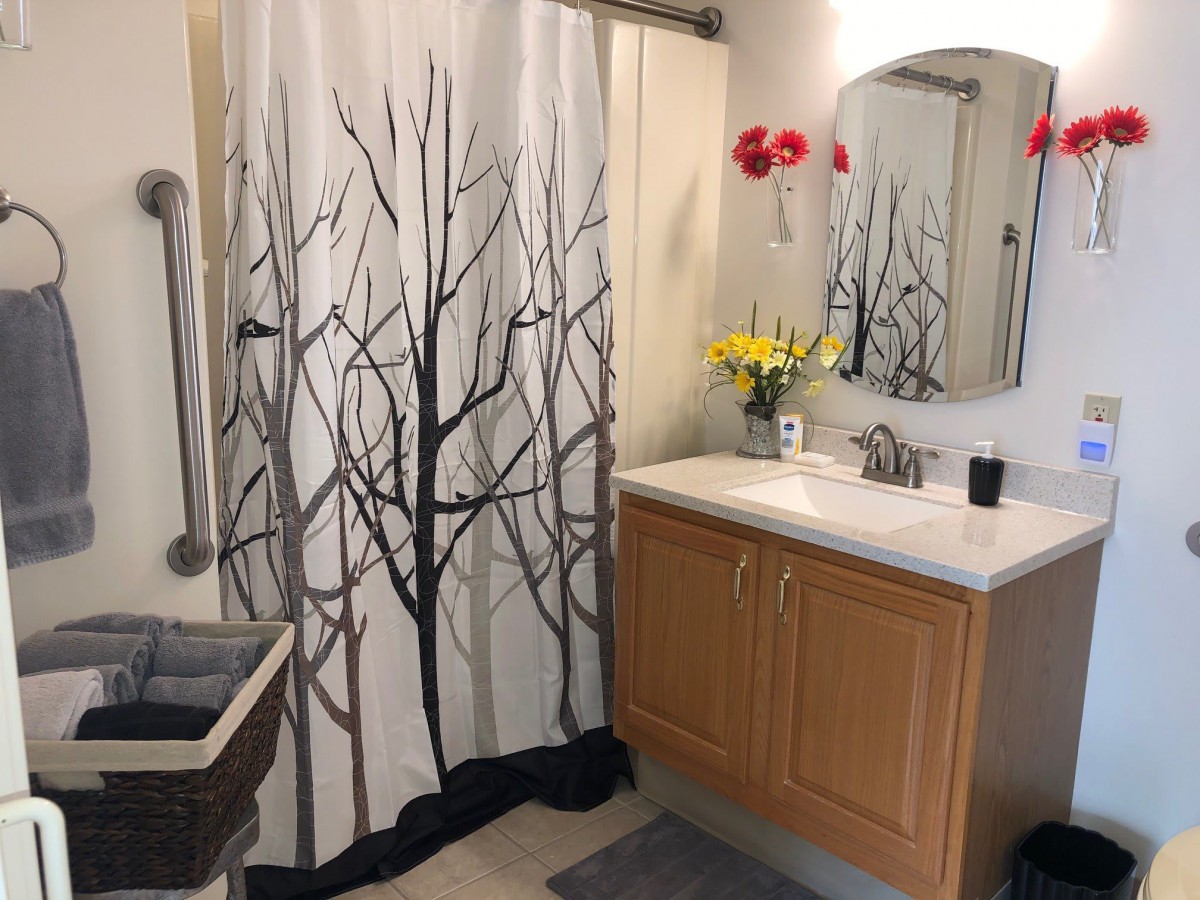 A neatly organized bathroom with a tree-themed shower curtain and fresh flowers on the vanity.