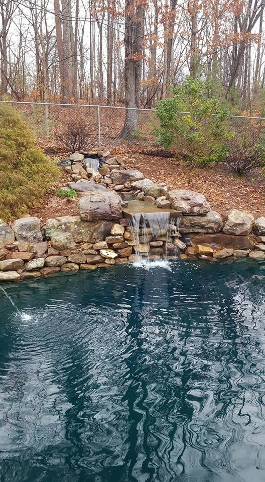 A serene pond with a small waterfall surrounded by rocks and natural foliage.
