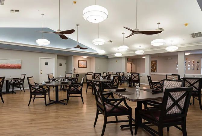 A well-lit dining area with wooden tables and chairs, ceiling fans, and a modern decor.