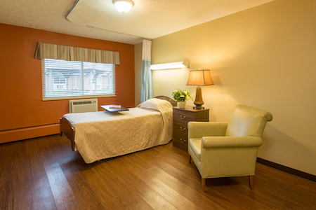 A cozy hospital room featuring a single bed, comfortable armchair, and warm lighting.