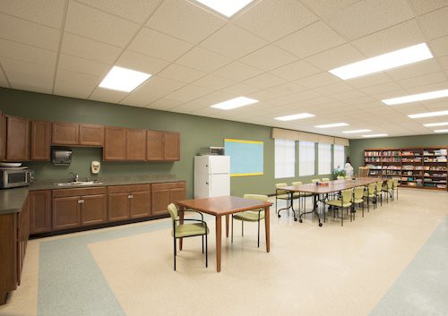 A modern classroom with tables, chairs, cabinets, and a whiteboard.