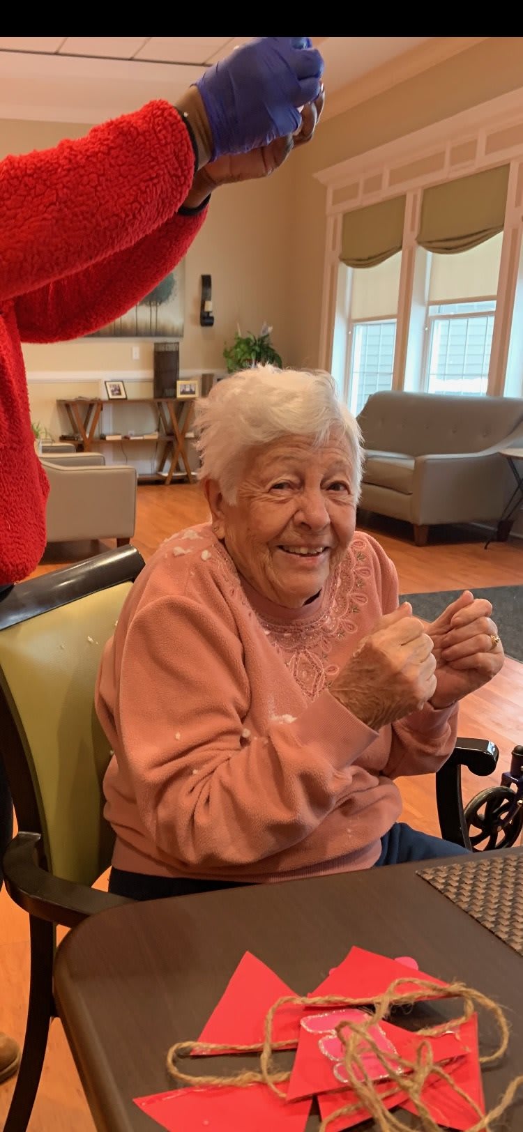 An elderly woman smiling while sitting in a wheelchair indoors.