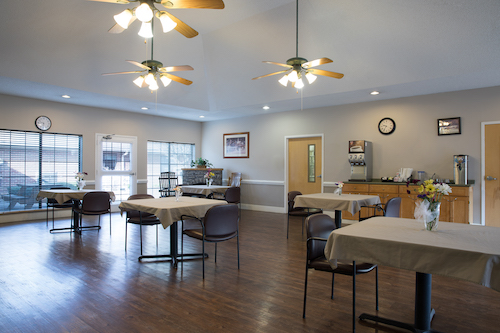 A spacious and inviting dining area featuring tables, chairs, and ceiling fans, designed for community gatherings.