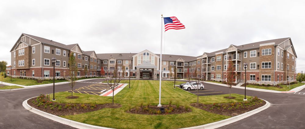 A large building with an American flag in front, featuring a neatly maintained lawn and parking area on a cloudy day.