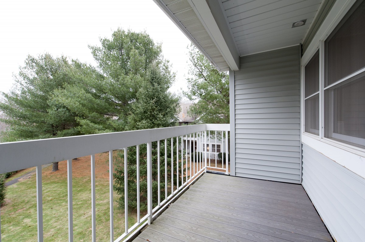 A balcony with white railings overlooking a yard with trees.