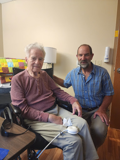 An elderly man shares a moment with his caregiver in a warm indoor setting.