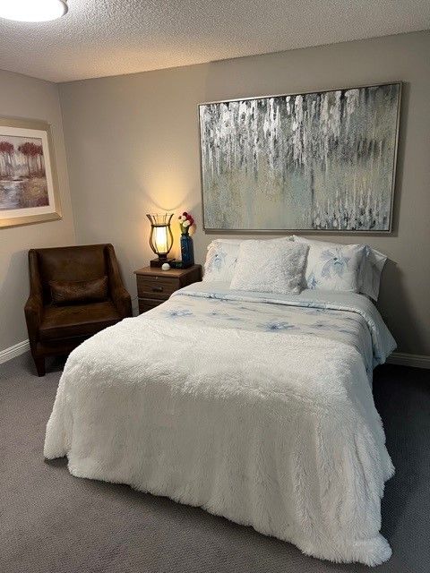A cozy bedroom with a bed, chair, lamp, and artwork on the walls.