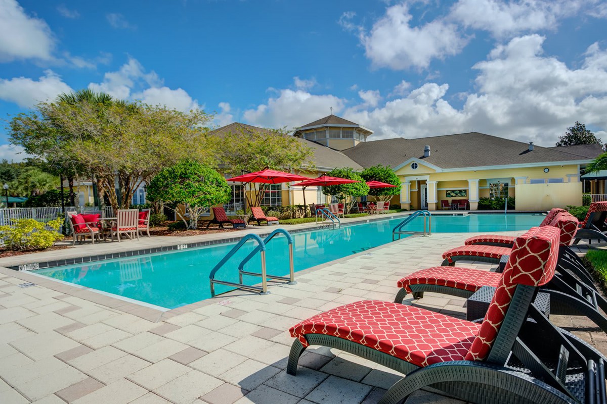 A tranquil outdoor swimming pool area with lounge chairs and red umbrellas, perfect for relaxation on a sunny day.