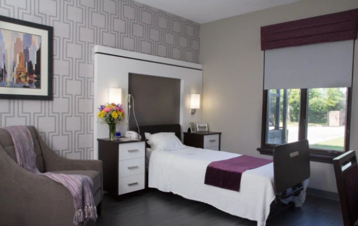 A modern hospital room with a single bed, stylish decor, and a flower arrangement on the nightstand.