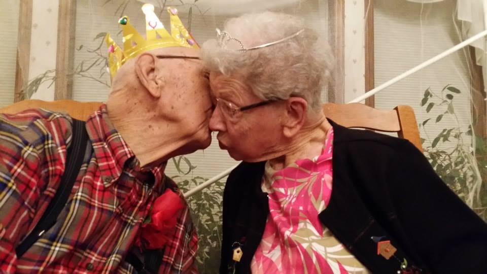 Elderly couple sharing a kiss while wearing crowns.