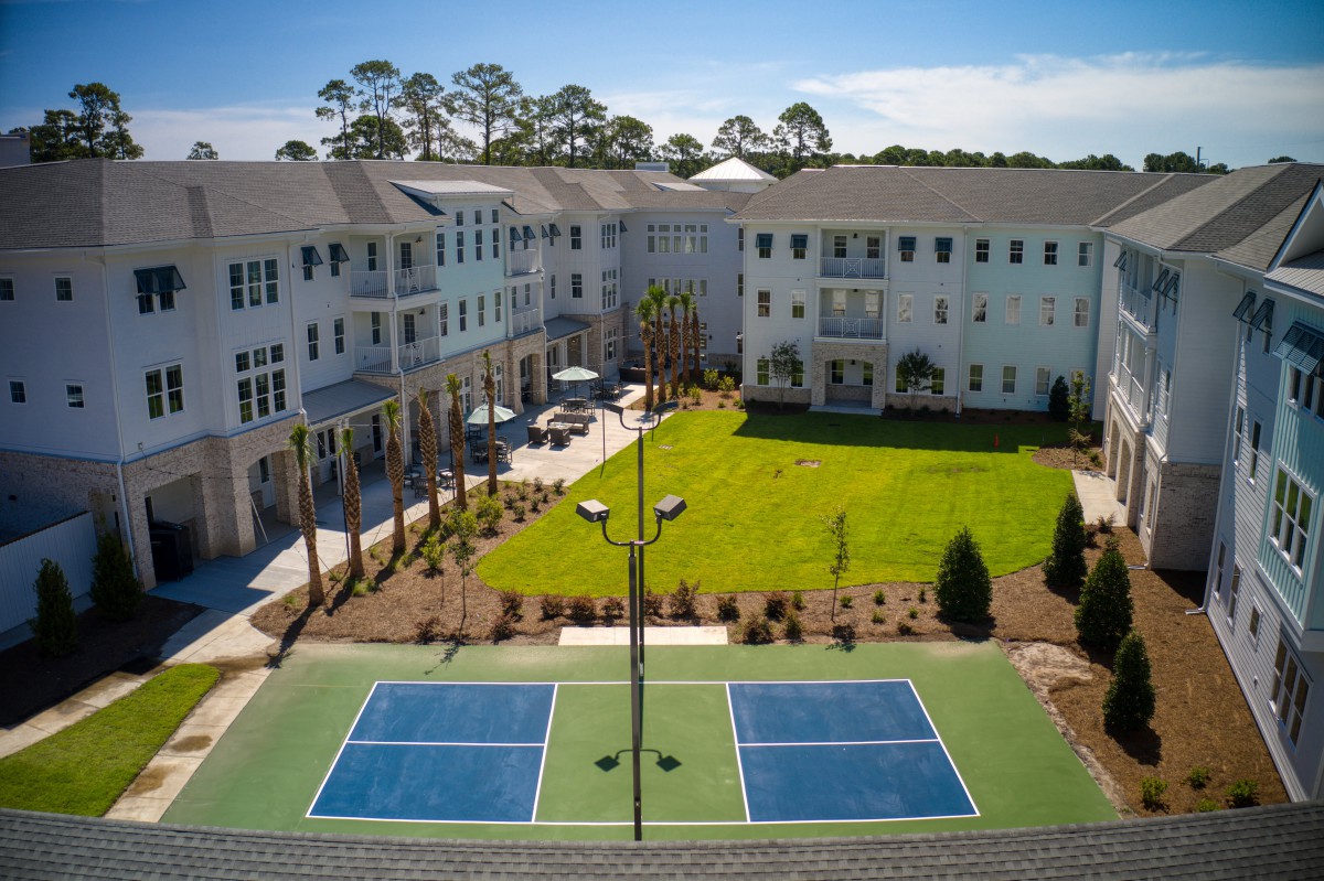 A residential apartment complex with a spacious courtyard, featuring a tennis court and landscaped green areas.