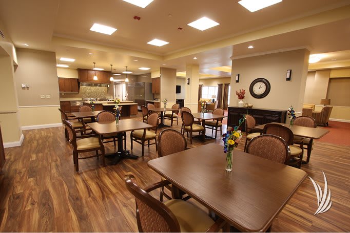 A spacious dining area with neatly arranged tables and chairs, featuring a kitchen in the background.