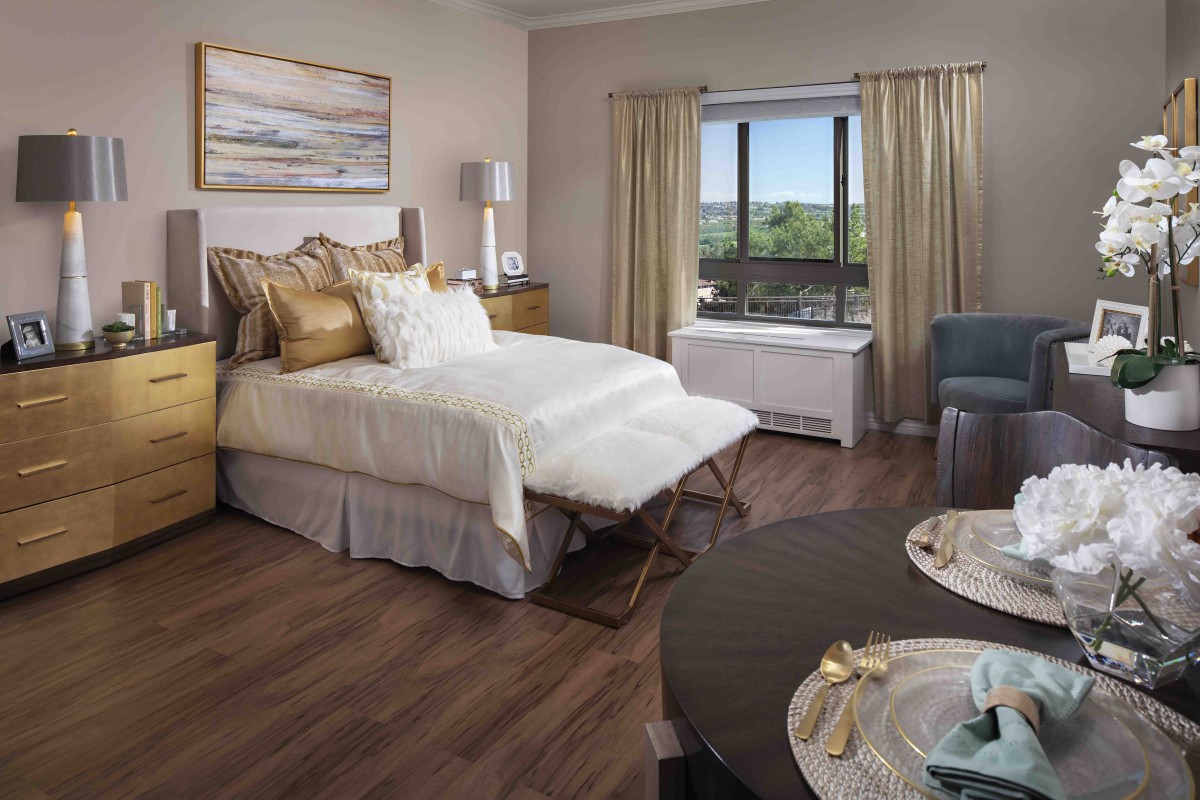 A cozy and well-decorated bedroom with a comfortable bed, stylish furniture, and a window with curtains offering a scenic view.