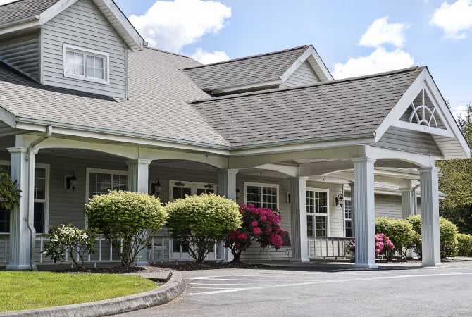 A suburban house with a front porch surrounded by landscaped bushes and flowers.