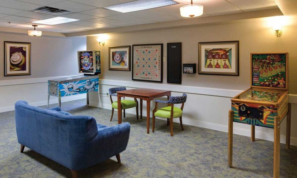 A cozy game room featuring a table and chairs, pinball machine, and wall art.