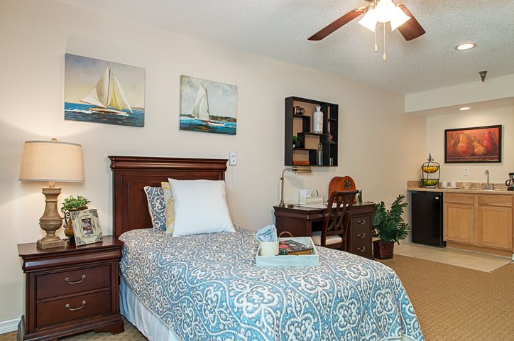 A cozy bedroom with a single bed, nautical artwork, and a ceiling fan.
