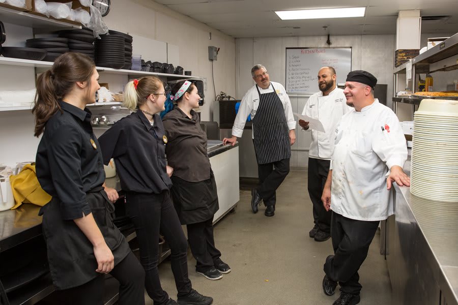 A group of chefs and kitchen staff having a discussion in the kitchen.