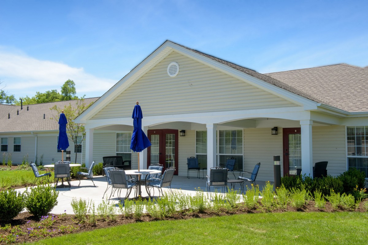 A well-maintained house with a spacious patio area featuring tables, chairs, and blue umbrellas.