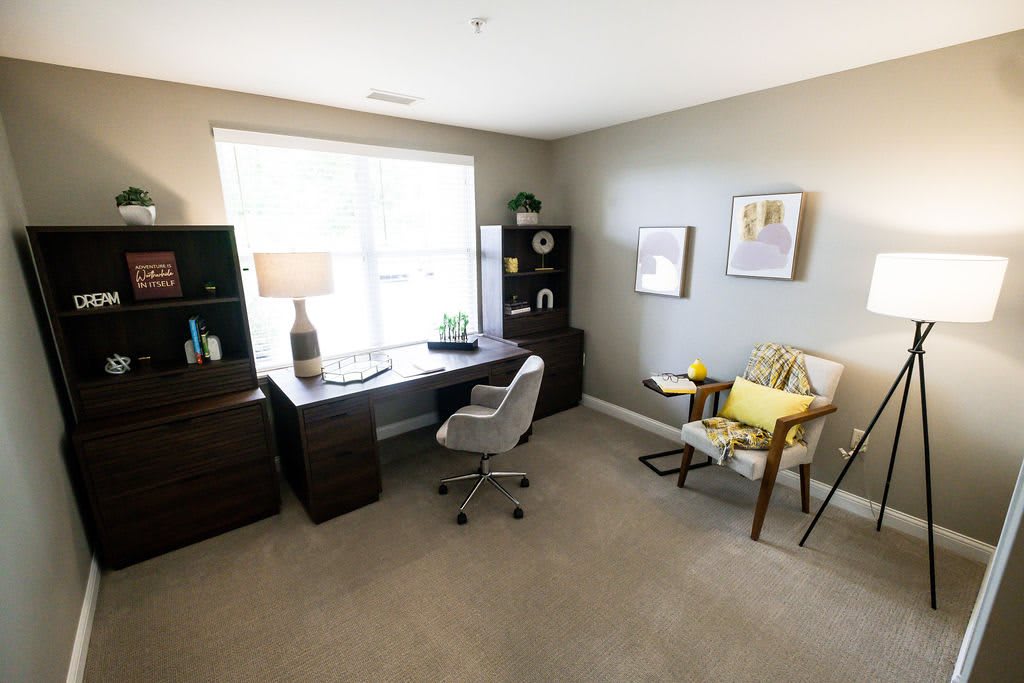 A bright and organized home office featuring a desk, chair, bookshelves, and decor, illuminated by natural light from a large window.