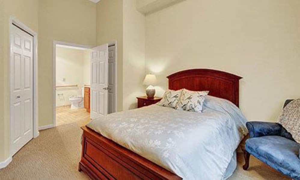A cozy bedroom with a wooden bed frame, bedside table, and lamp, connected to a bathroom.