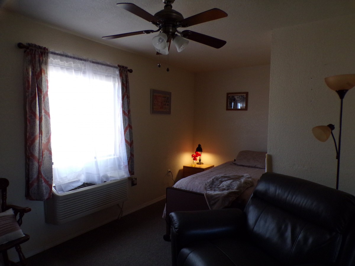 A cozy bedroom with a single bed, armchair, and a lit lamp next to the window with curtains.
