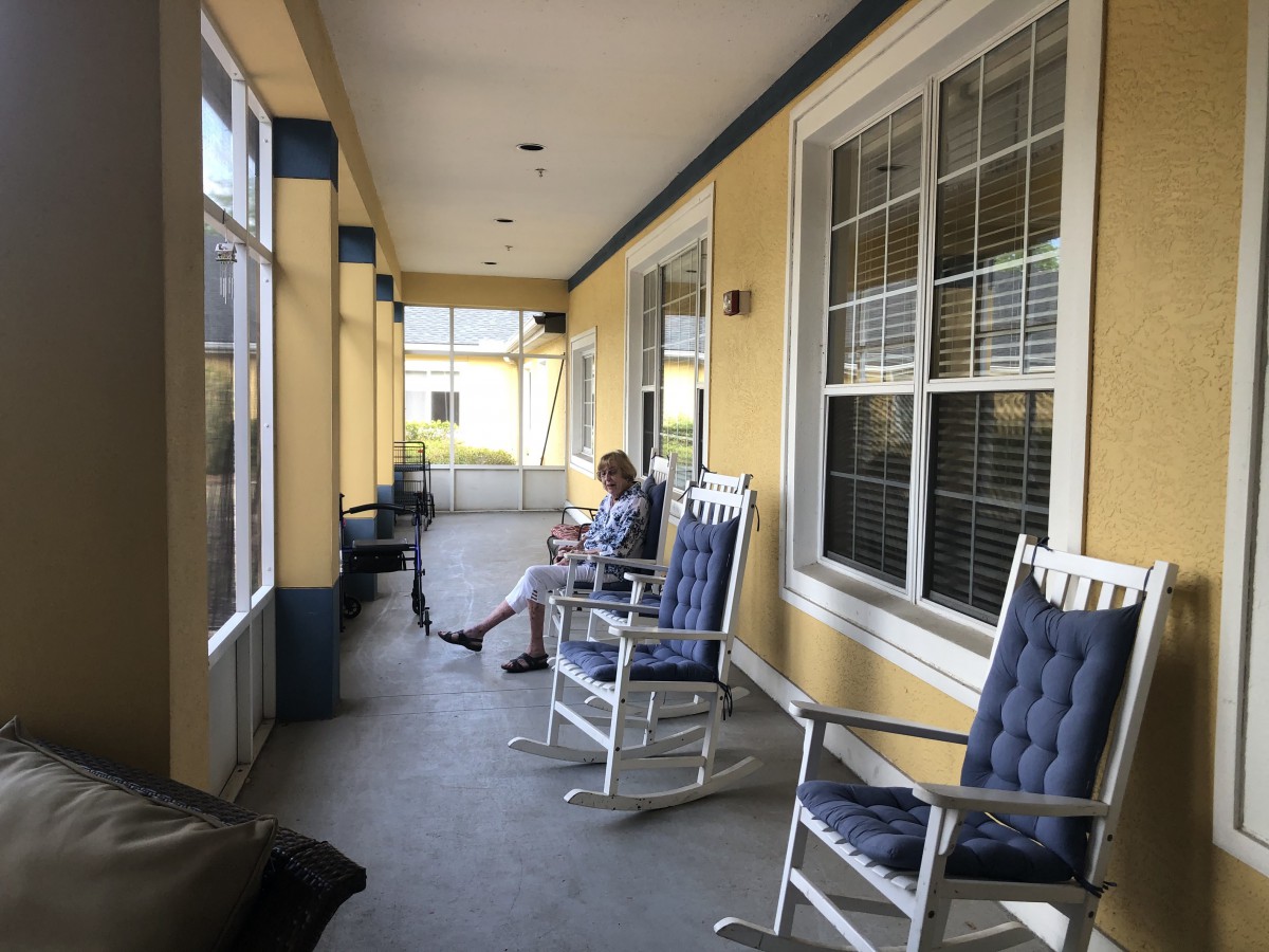 A person sitting on a porch with several rocking chairs.