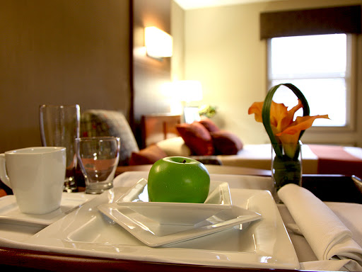 A neatly arranged breakfast tray featuring a green apple and a small bouquet of flowers, set in a cozy hotel room.