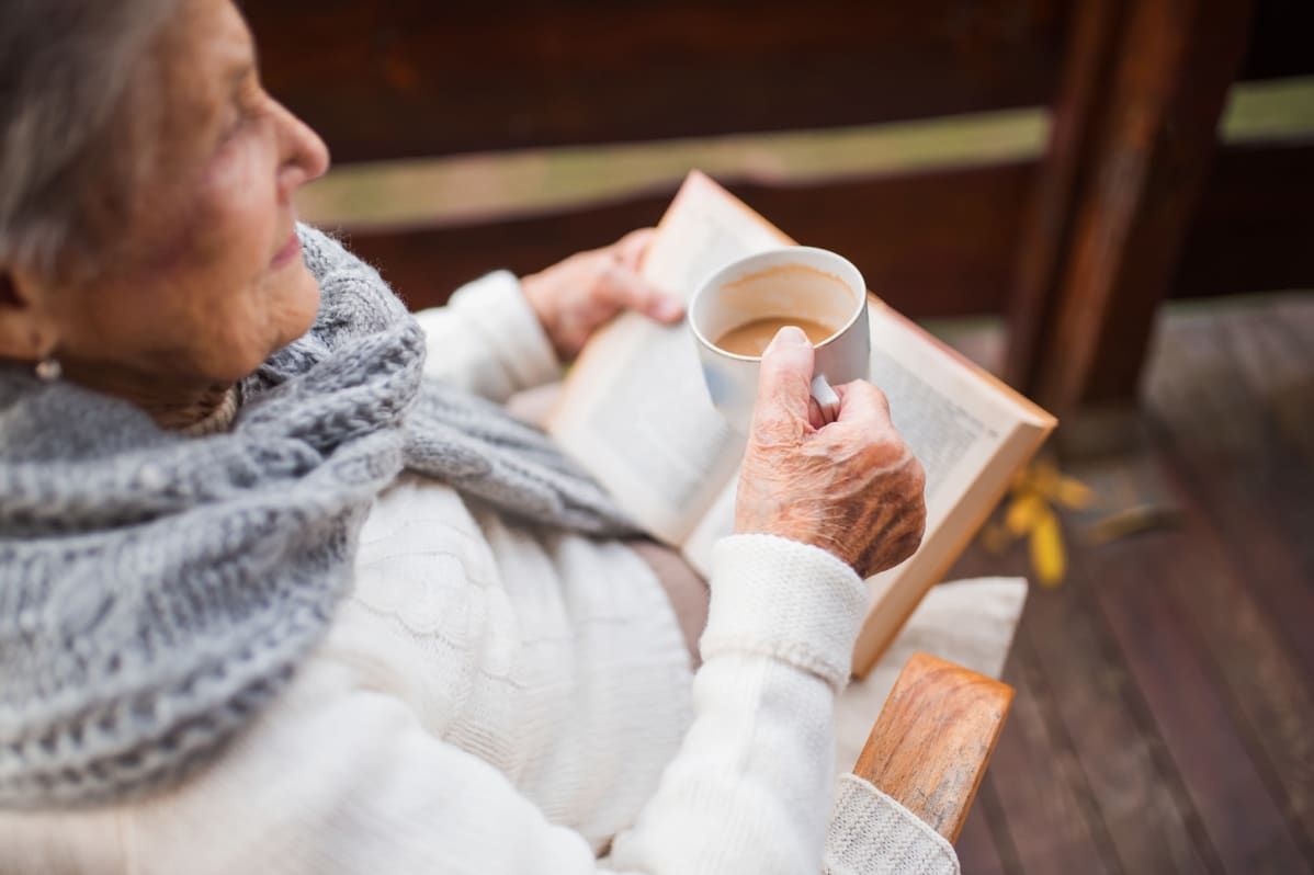 An elderly person relaxing indoors, enjoying a book and a cup of coffee.