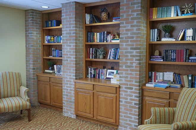 A cozy library corner featuring wooden bookshelves integrated into a brick wall, filled with various books and decorative items.
