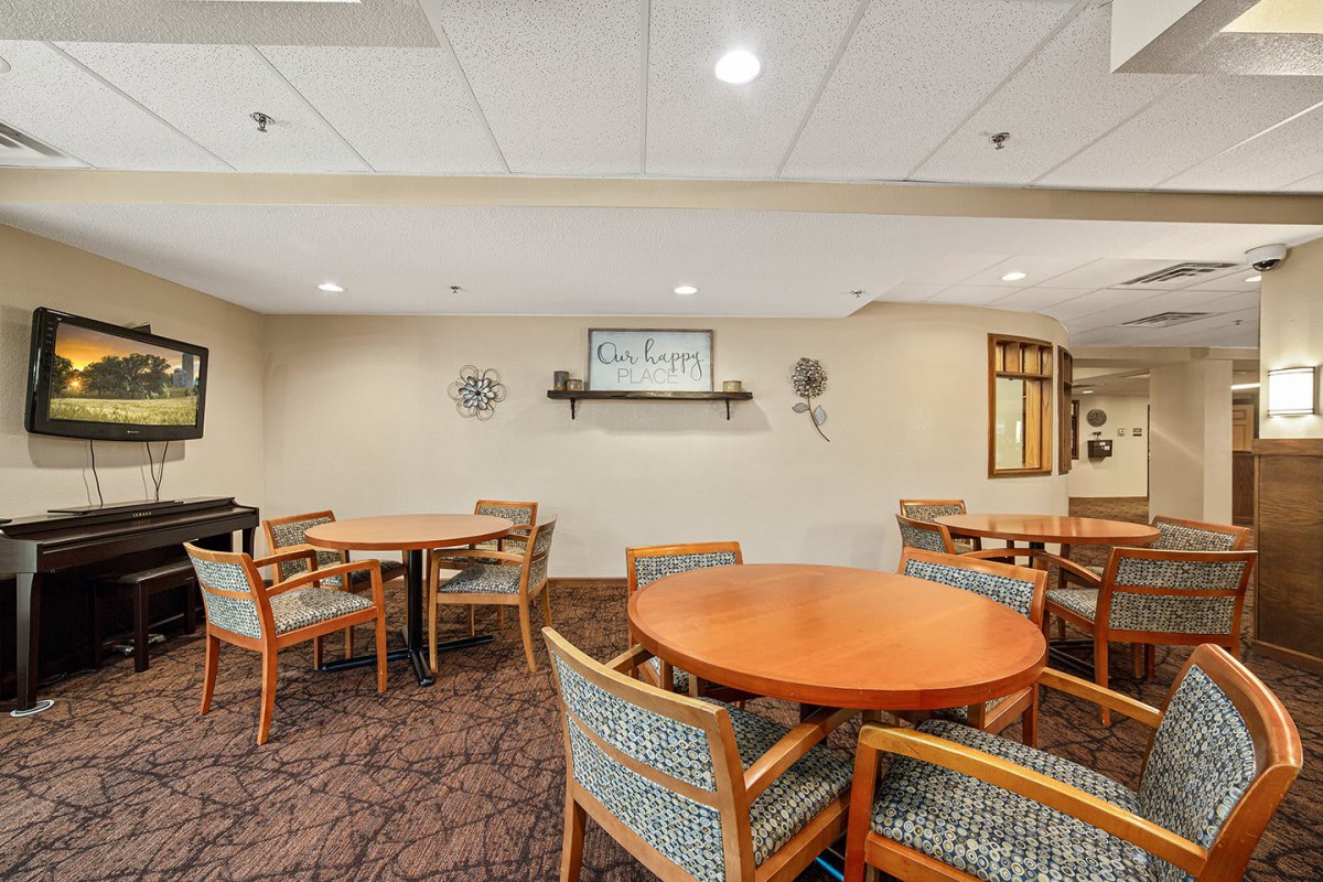 A cozy dining area with round tables and upholstered chairs arranged on a carpeted floor.