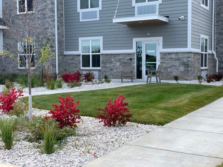 A beautifully landscaped garden with red shrubs and a green lawn in front of a house with a stone facade.