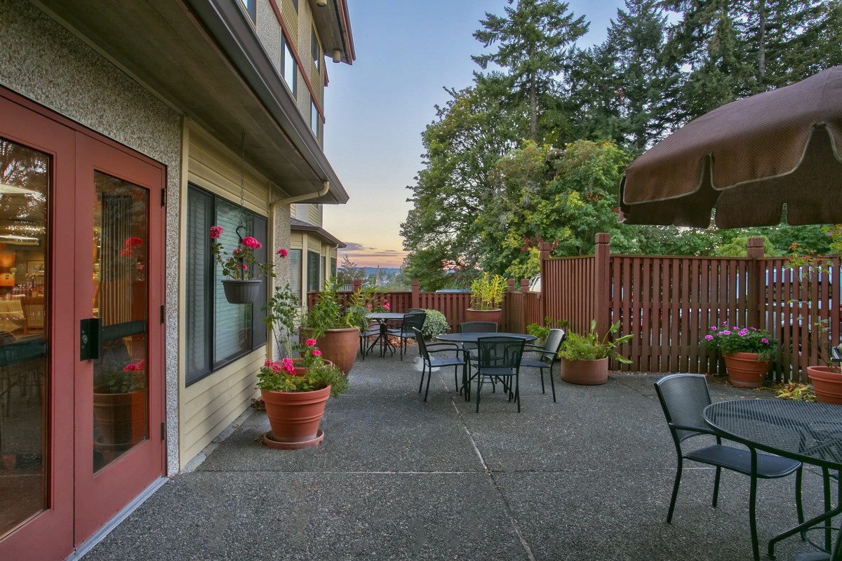 A cozy outdoor patio with tables, chairs, and potted plants surrounded by a wooden fence in the evening.
