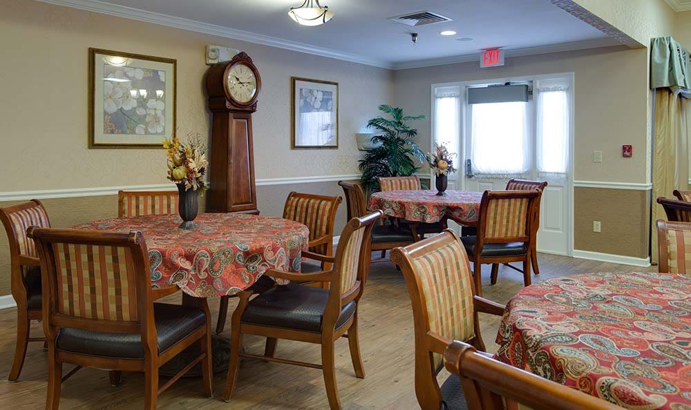 A cozy dining room with decorated tables, wooden chairs, a grandfather clock, and framed wall art.