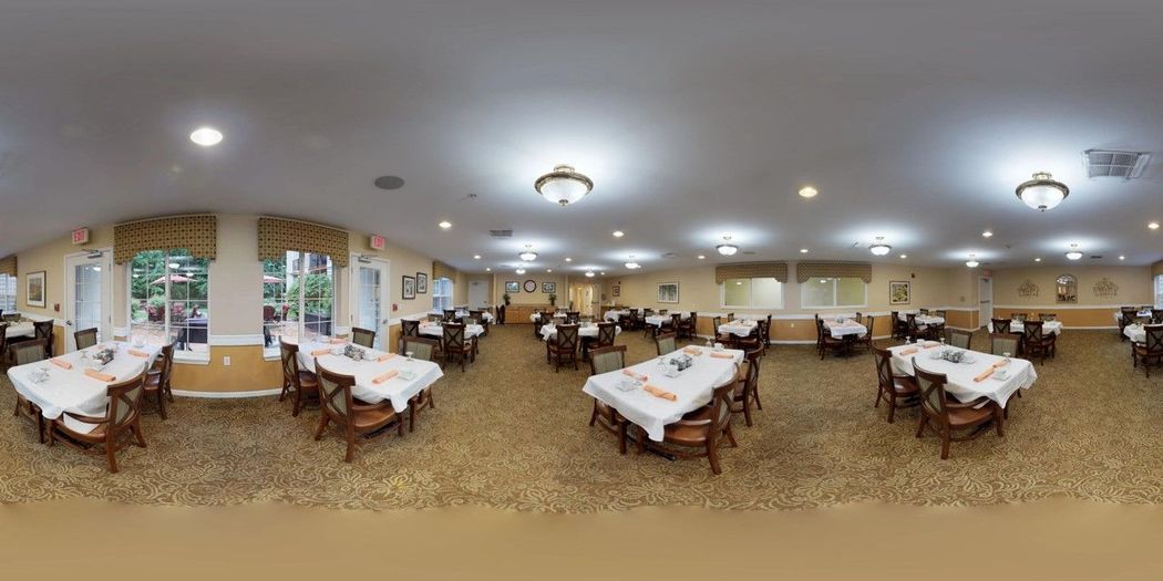 A well-lit dining room with multiple tables set up with white tablecloths.