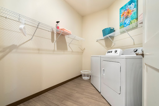 A tidy laundry room featuring a washing machine, dryer, and organized shelves with towels and cleaning supplies.