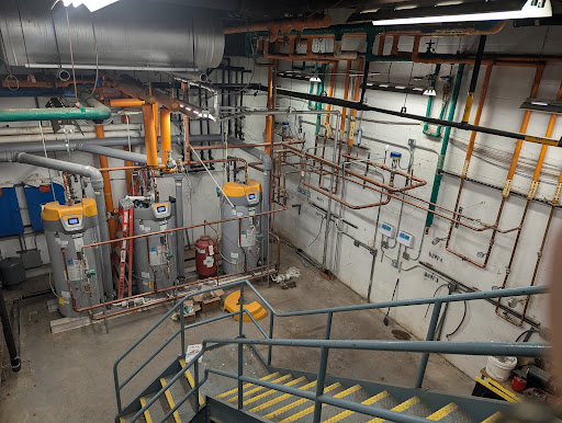 An industrial space showcasing an array of pipes and mechanical equipment, alongside a staircase.