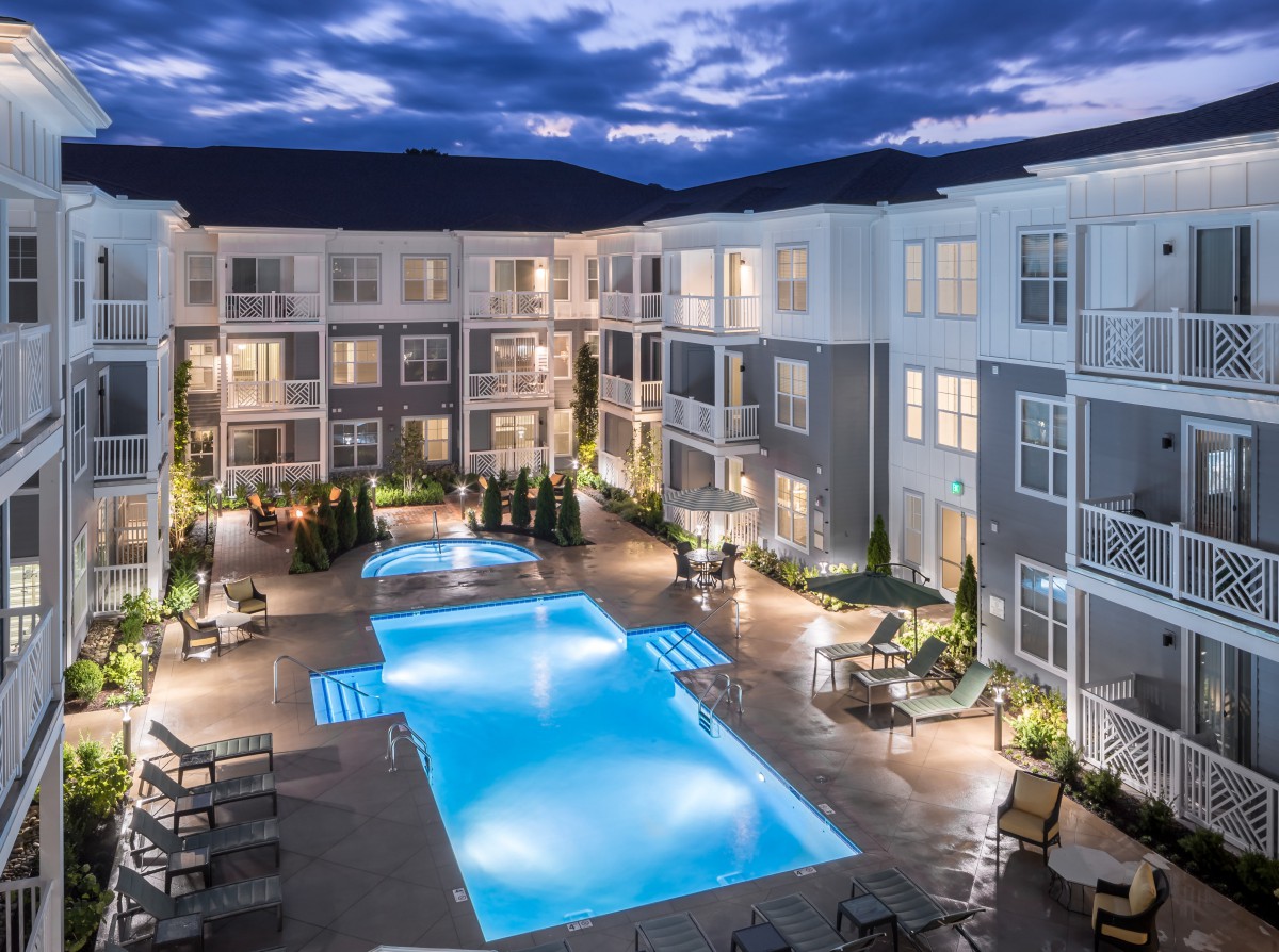 A modern apartment complex with a brightly lit swimming pool at night.
