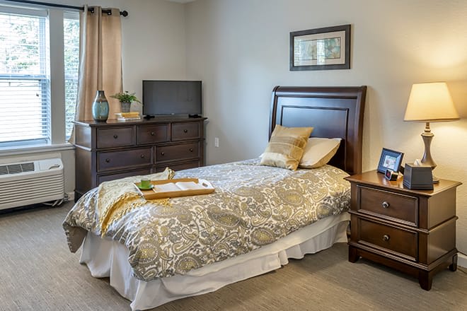 A cozy bedroom with a single bed, dresser, and television.