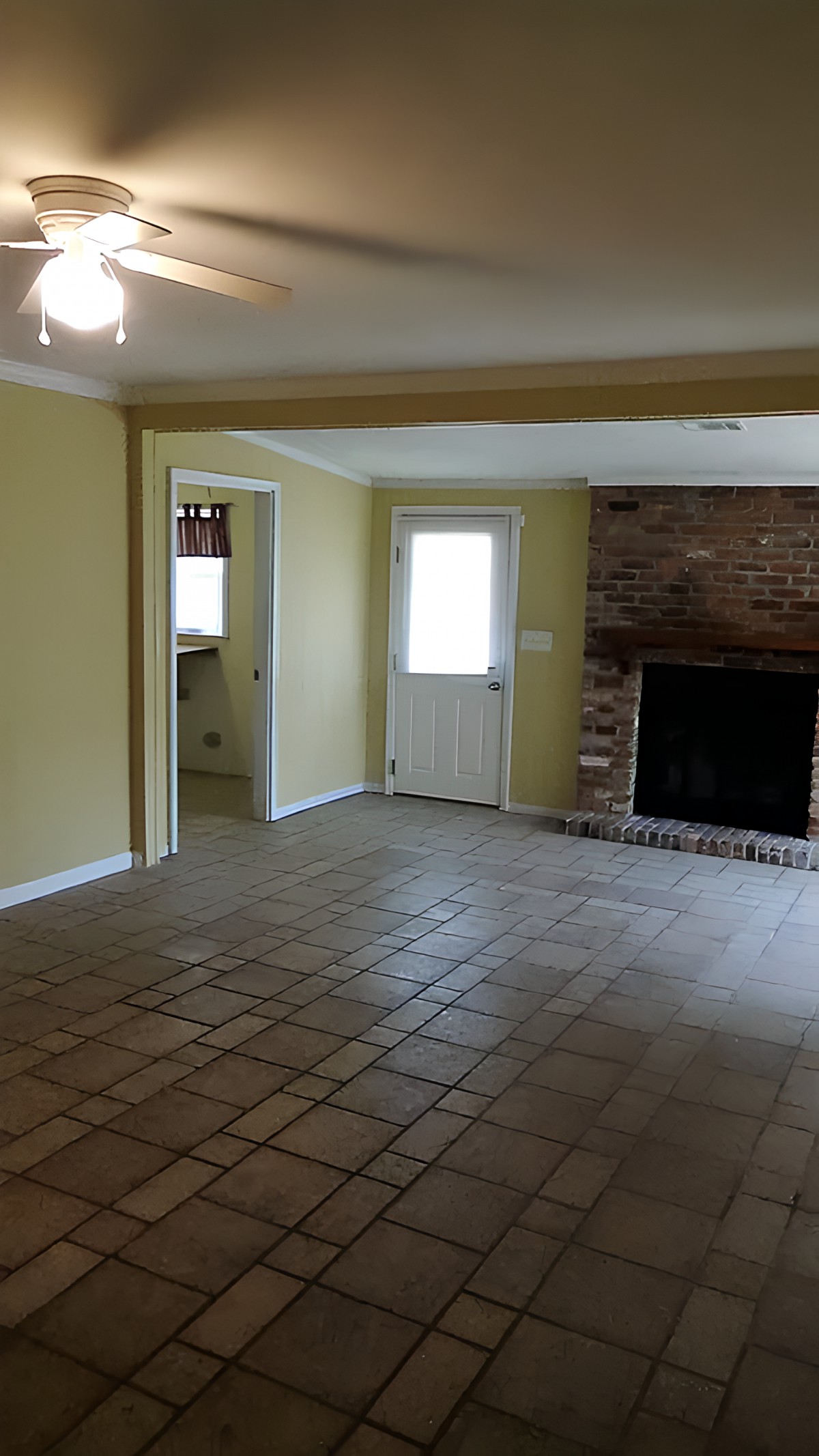 An empty room featuring a brick fireplace and tiled floors, with a door leading to another space.