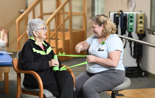A healthcare professional assists an elderly patient with resistance band exercises during a physiotherapy session.