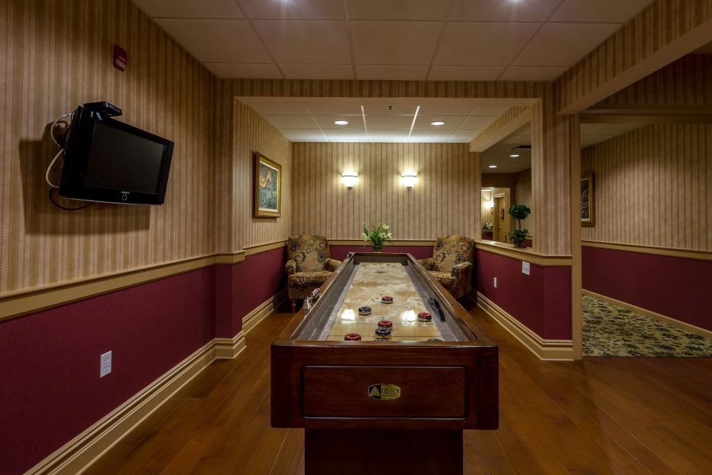 A cozy game room featuring a shuffleboard table, lounge chairs, and a wall-mounted TV.