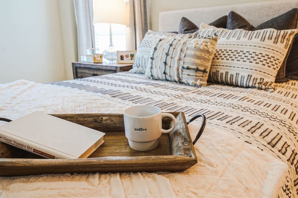 A cozy bedroom with a tray holding a mug and book on the bed.
