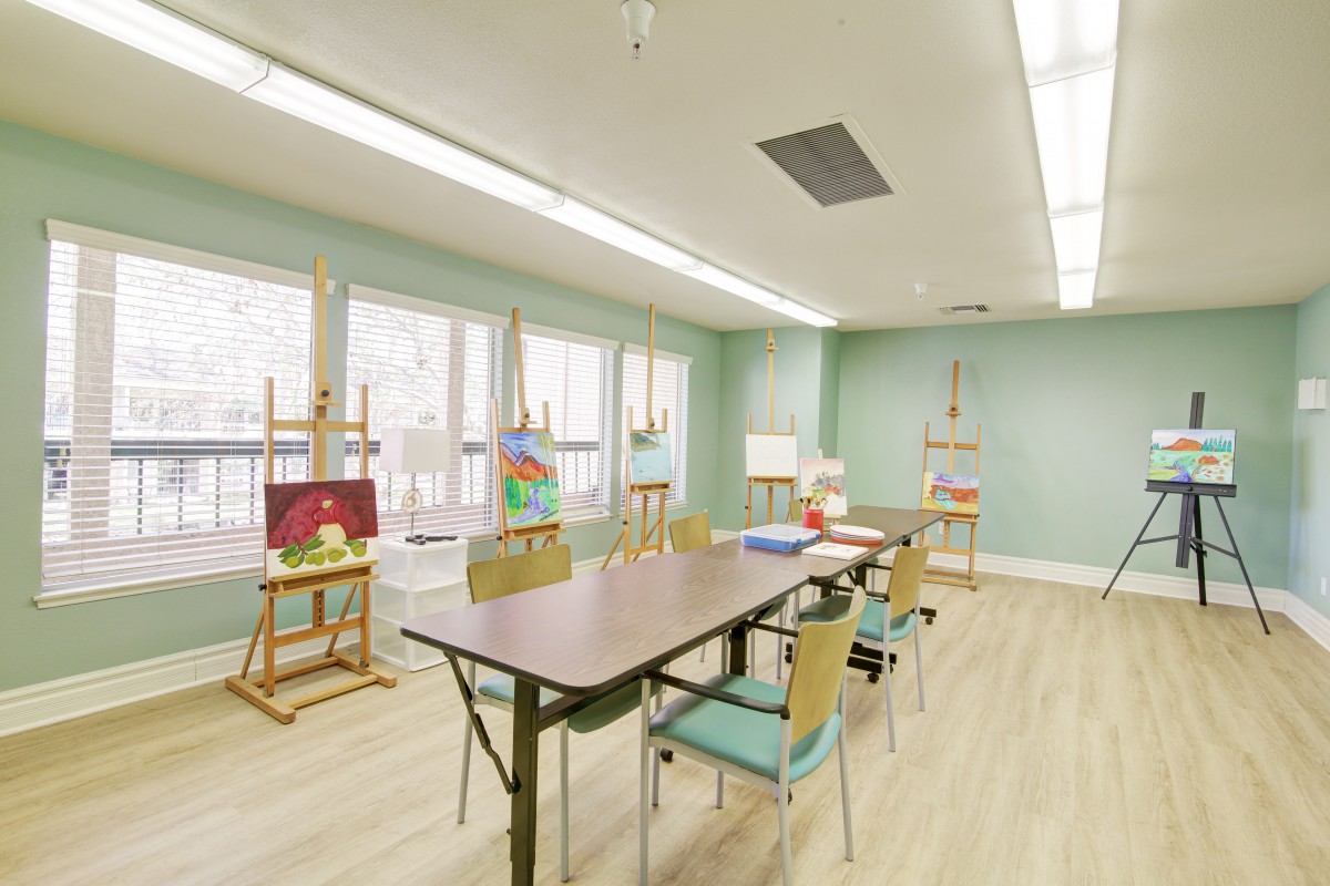 A spacious art classroom with tables, chairs, and easels near large windows.