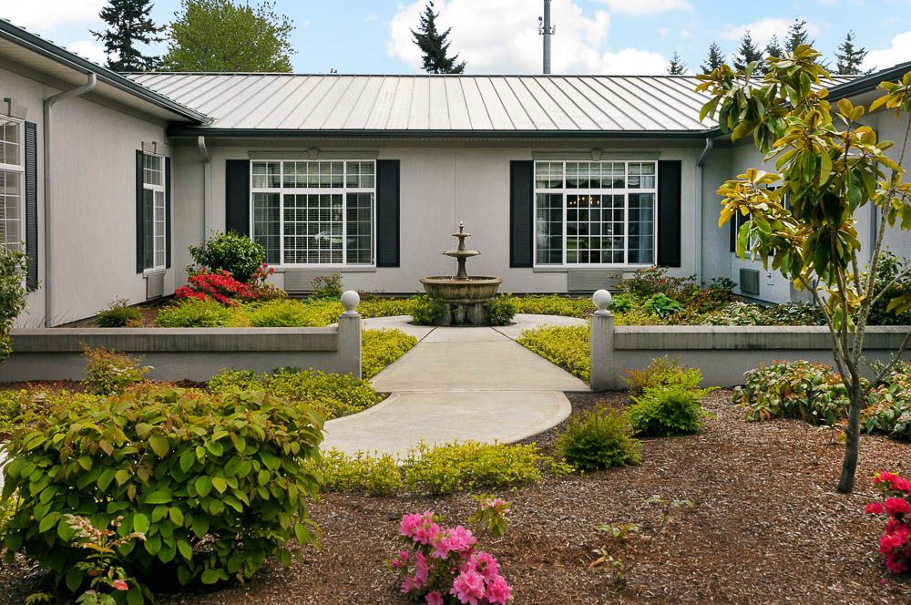 A house with a well-maintained garden, featuring a central fountain and pathway surrounded by shrubs and flowers.