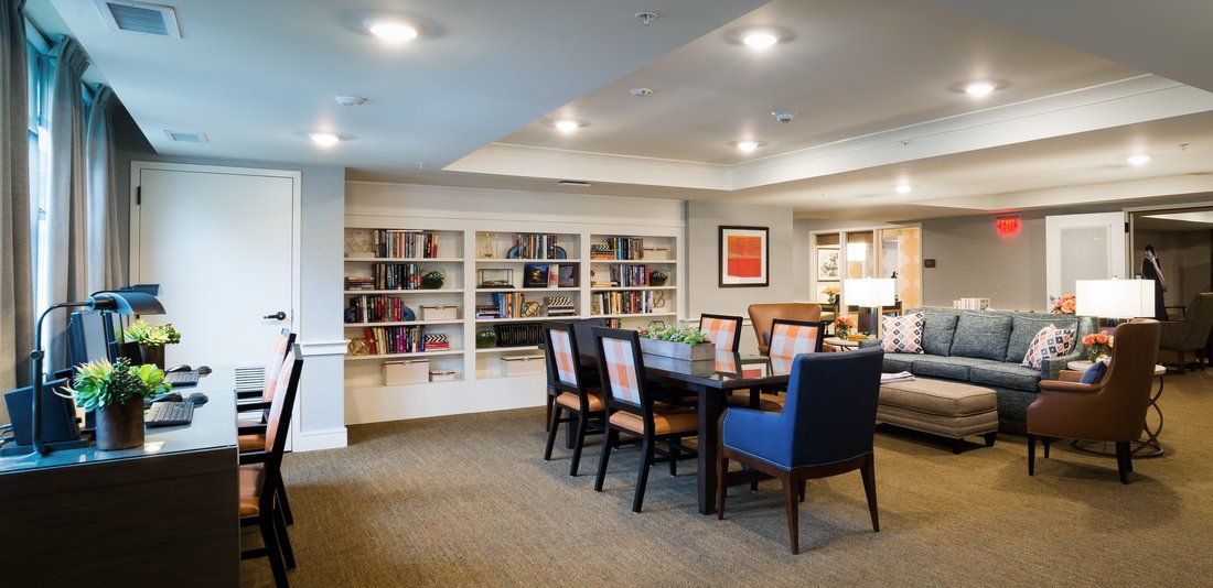 A cozy library space with bookshelves, a large table, and comfortable chairs.