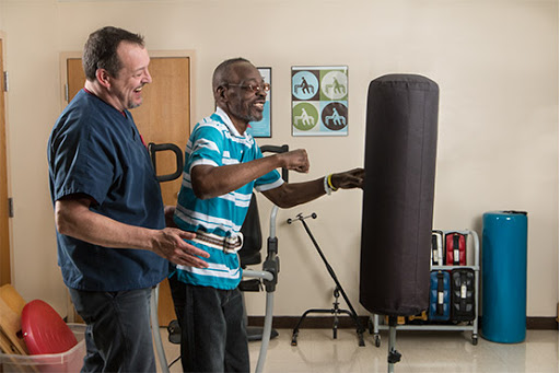 A senior citizen engages in a boxing exercise with the assistance of a caregiver, promoting fitness and rehabilitation.