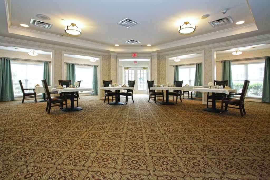 A spacious dining room with several tables and chairs arranged on a patterned carpeted floor.