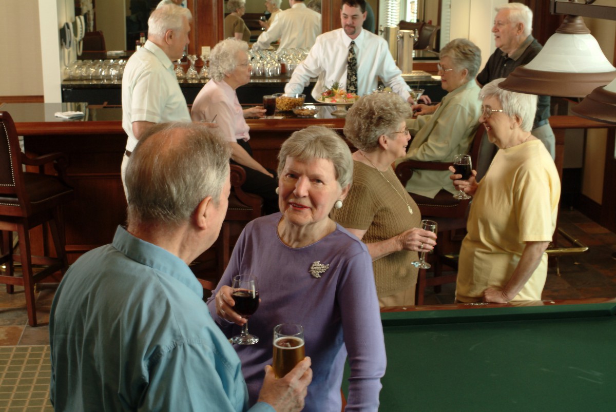A group of seniors enjoying a social gathering at a bar, engaged in conversation and holding drinks.