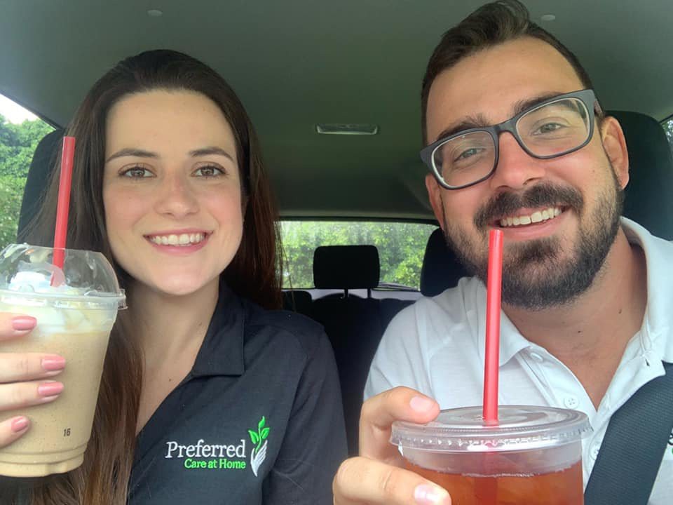 Two people sitting in a car, smiling and holding drinks.